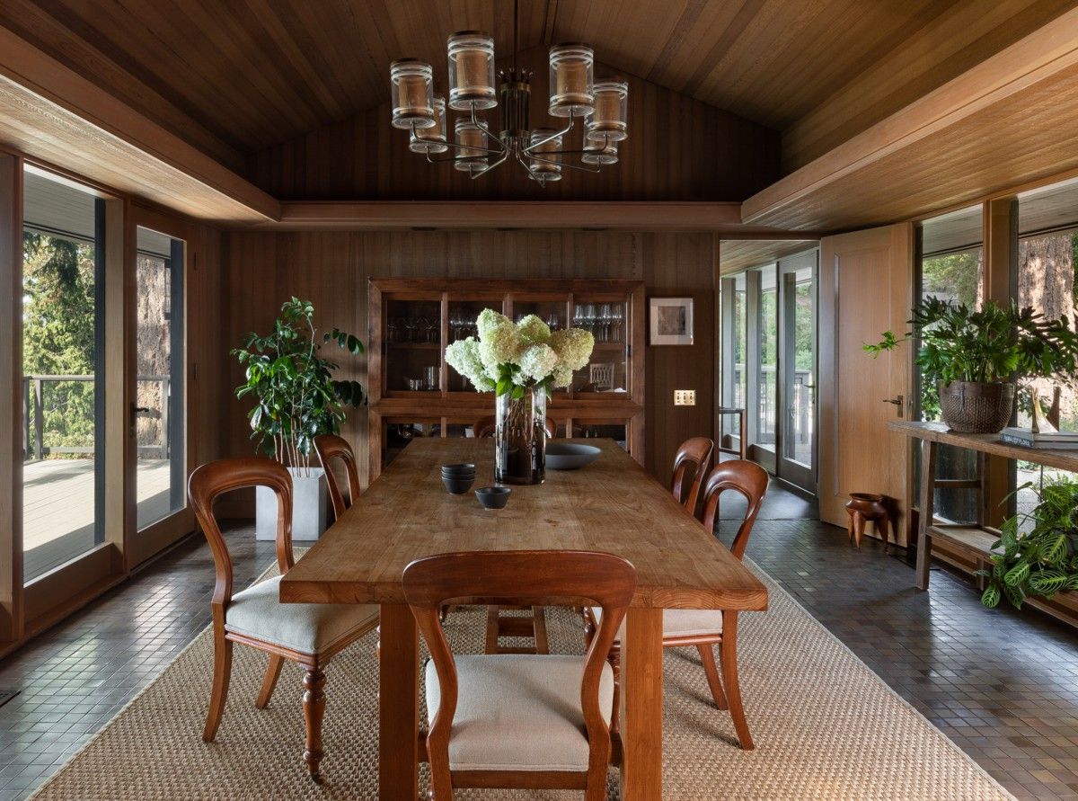 Cabin-style dining room of the house is connected with the outdoors using glass walls