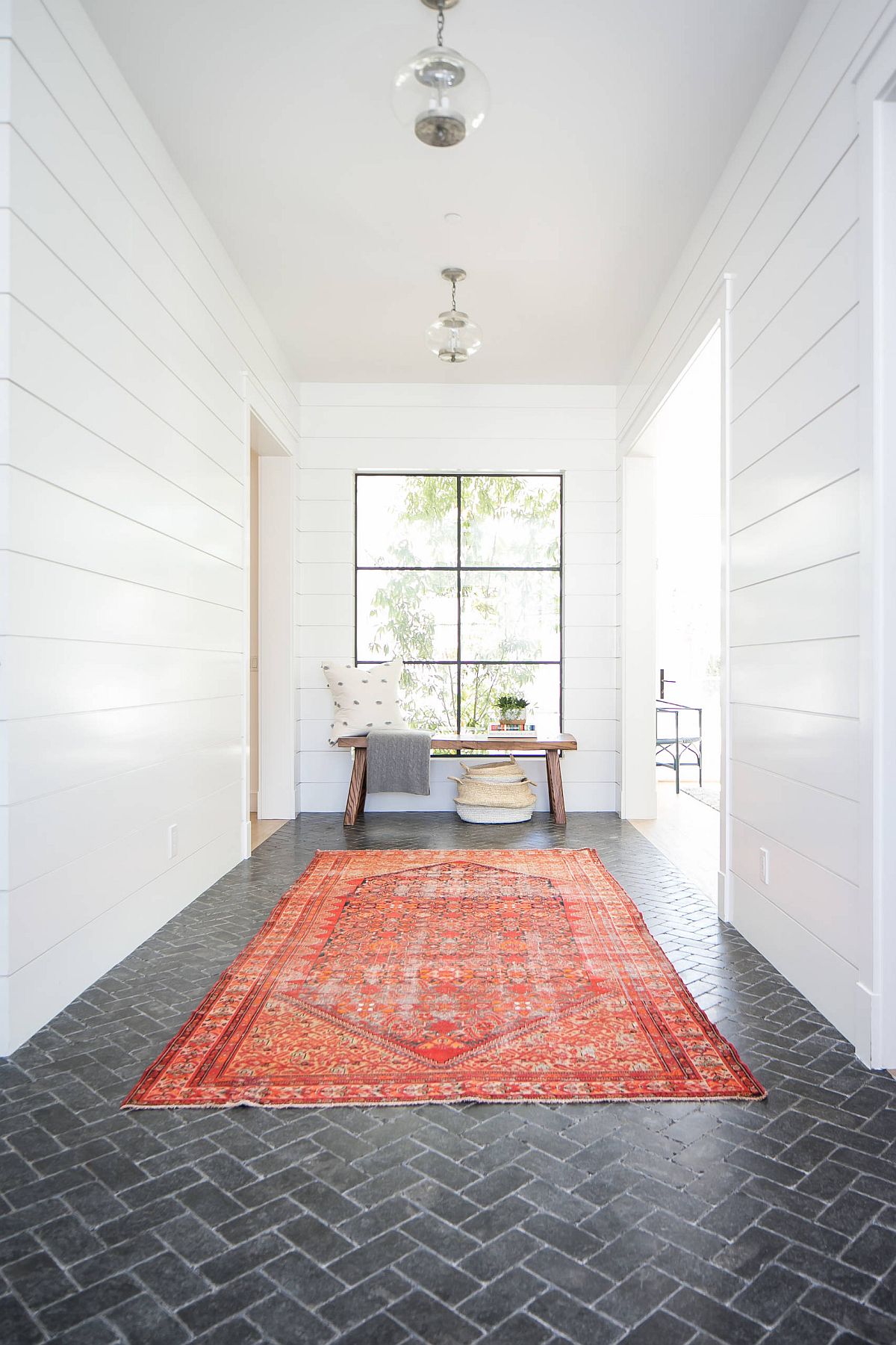 Rug adds bright orange hue to the neutral modern entry that has white walls and dark gray brick floor