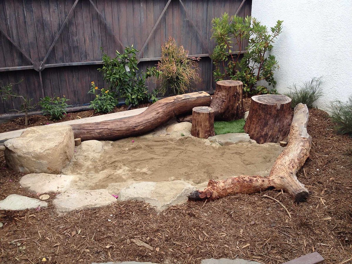 Rustic backyard play area with a sandbox that is surrounded by tree trunks and wooden logs