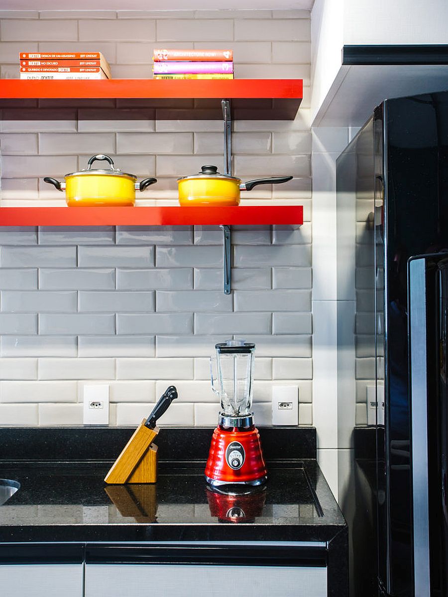 Sleek floating shelves in orange add color to the white-tiled kitchen backsplash