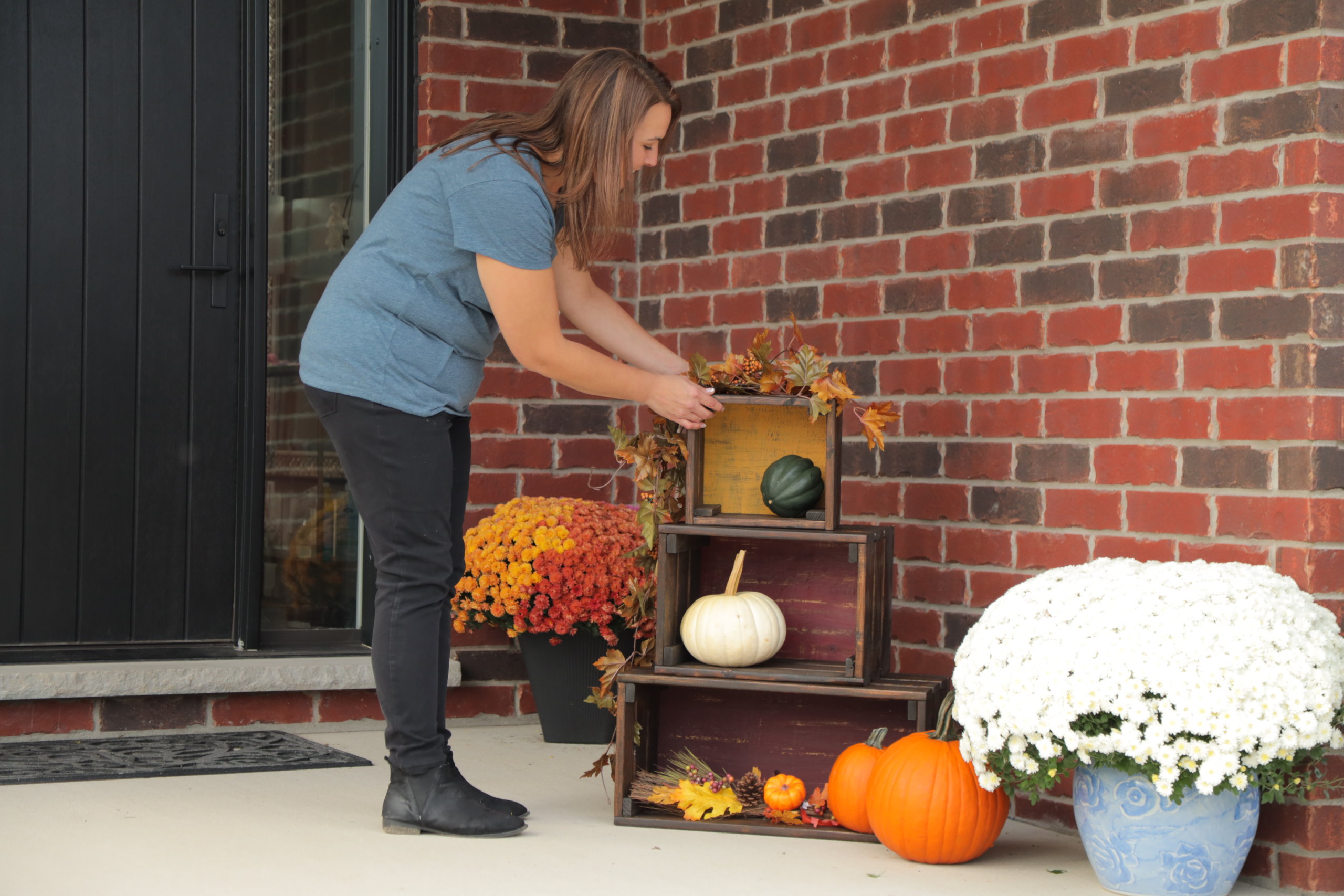 woman sets up fall porch display with wood crates and pumpkins