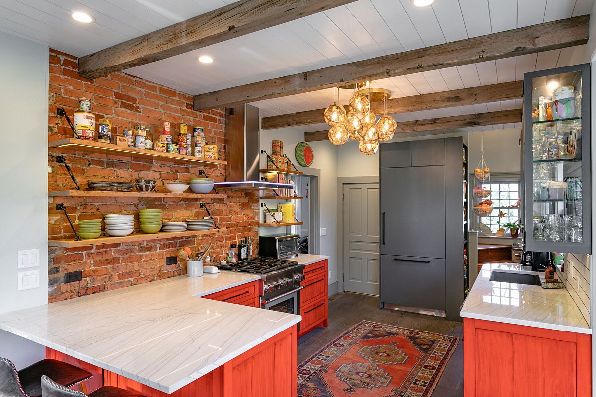 Beautiful farmhouse kitchen with exposed brick wall section and cabinets in brick red with an orangish tinge