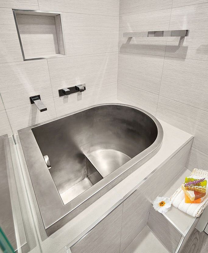 Metallic soaking tub is integrated with the bathroom design and features a comfortable space to sit