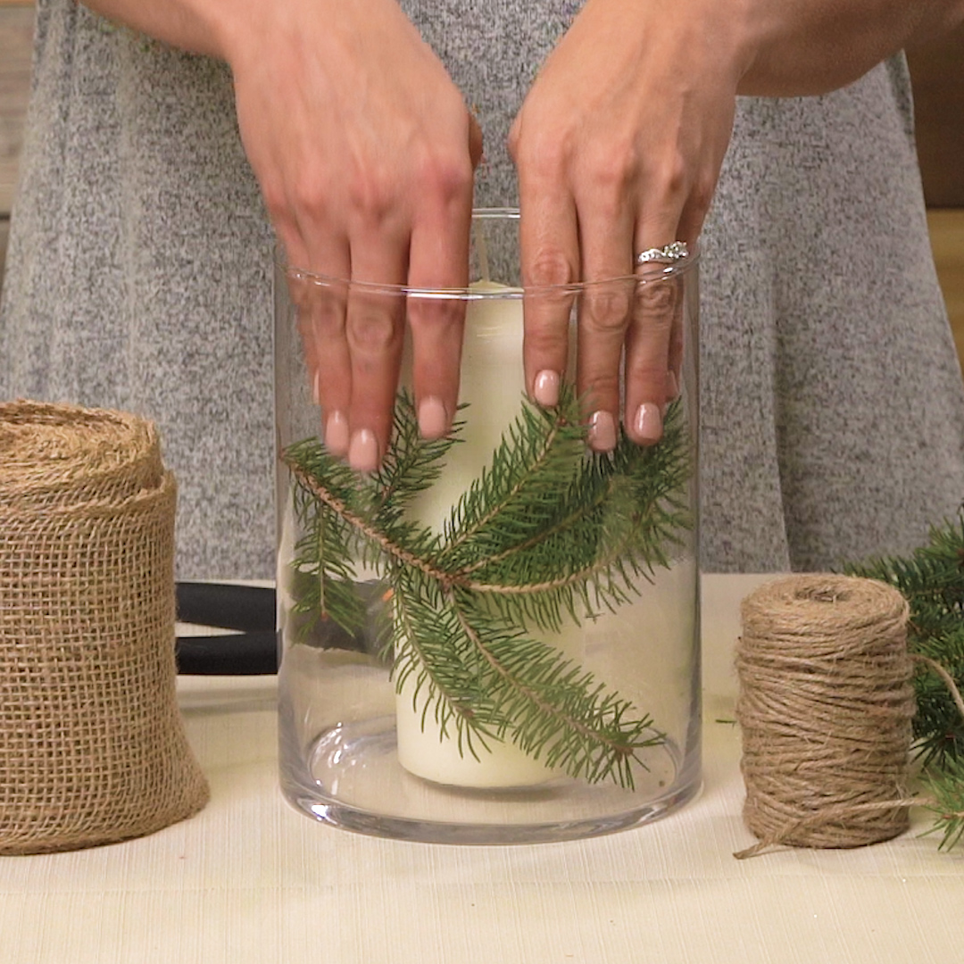 placing evergreen clippings around candle in vase