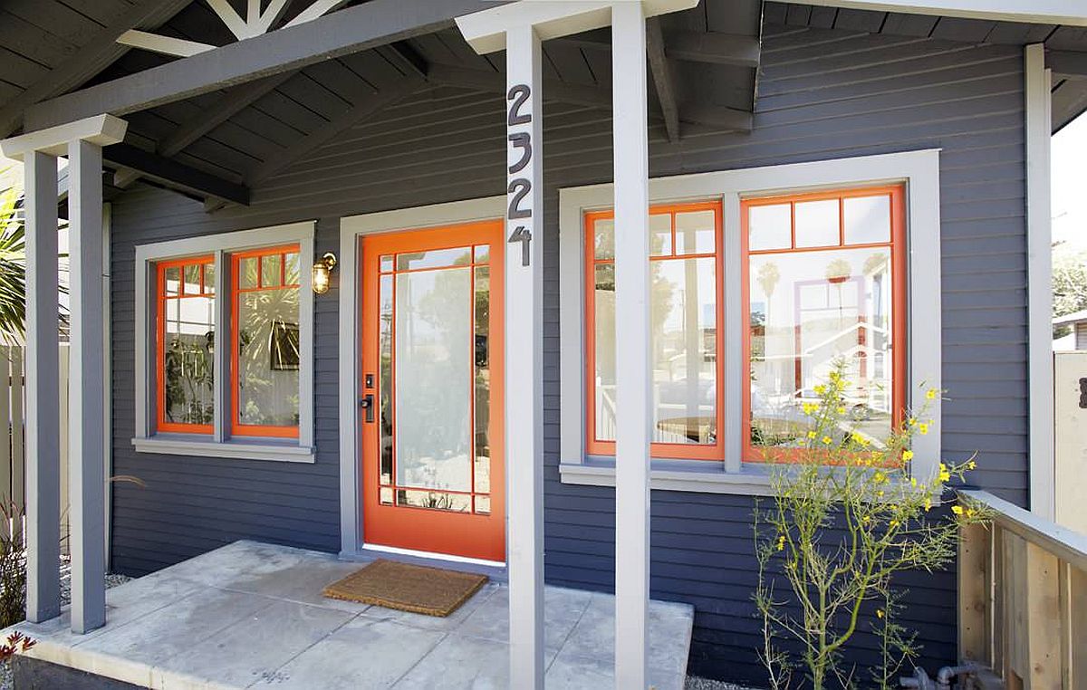 Orange door and window frames bring brightness to this dark gray home exterior