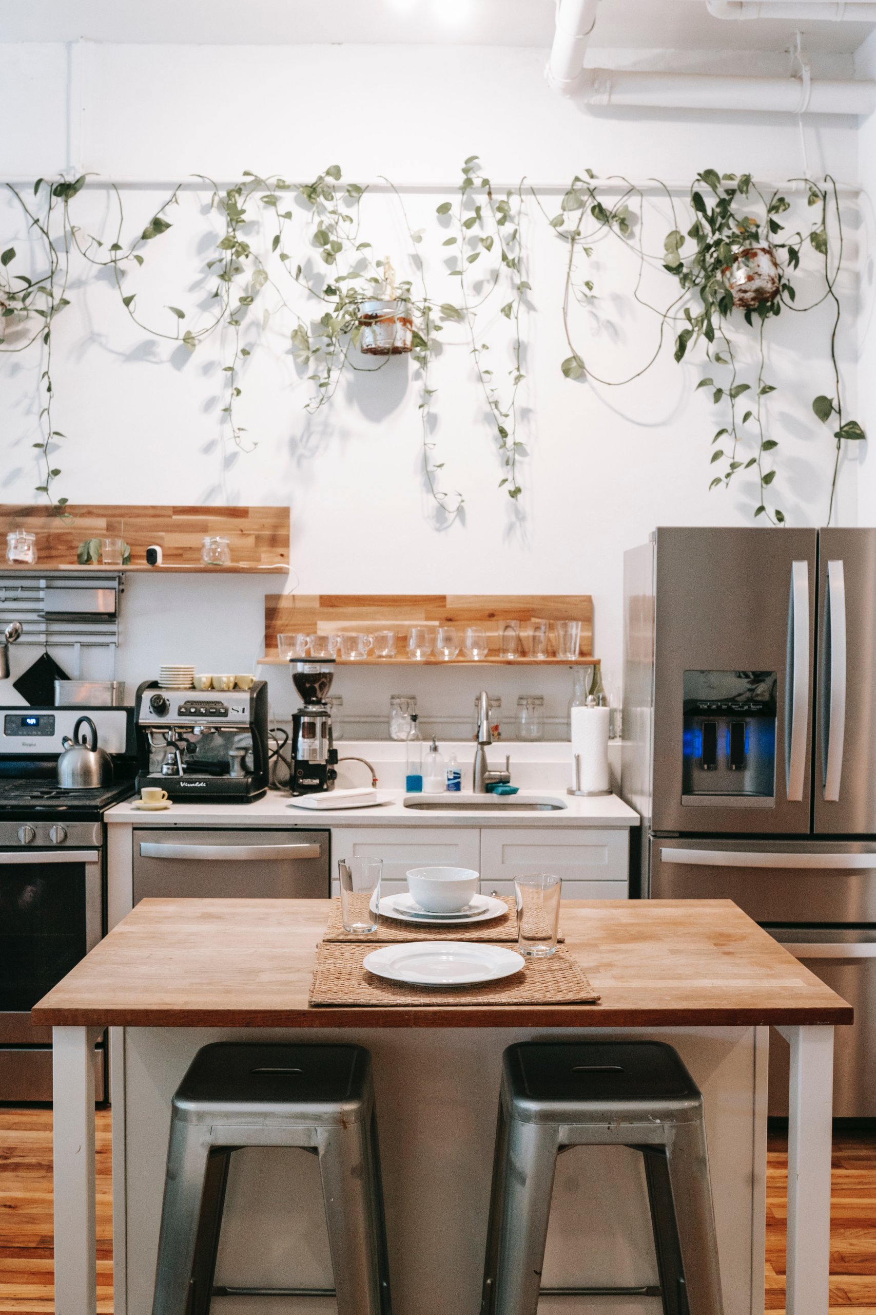 Brown dining table with two silver chairs and hanging plants on the wall