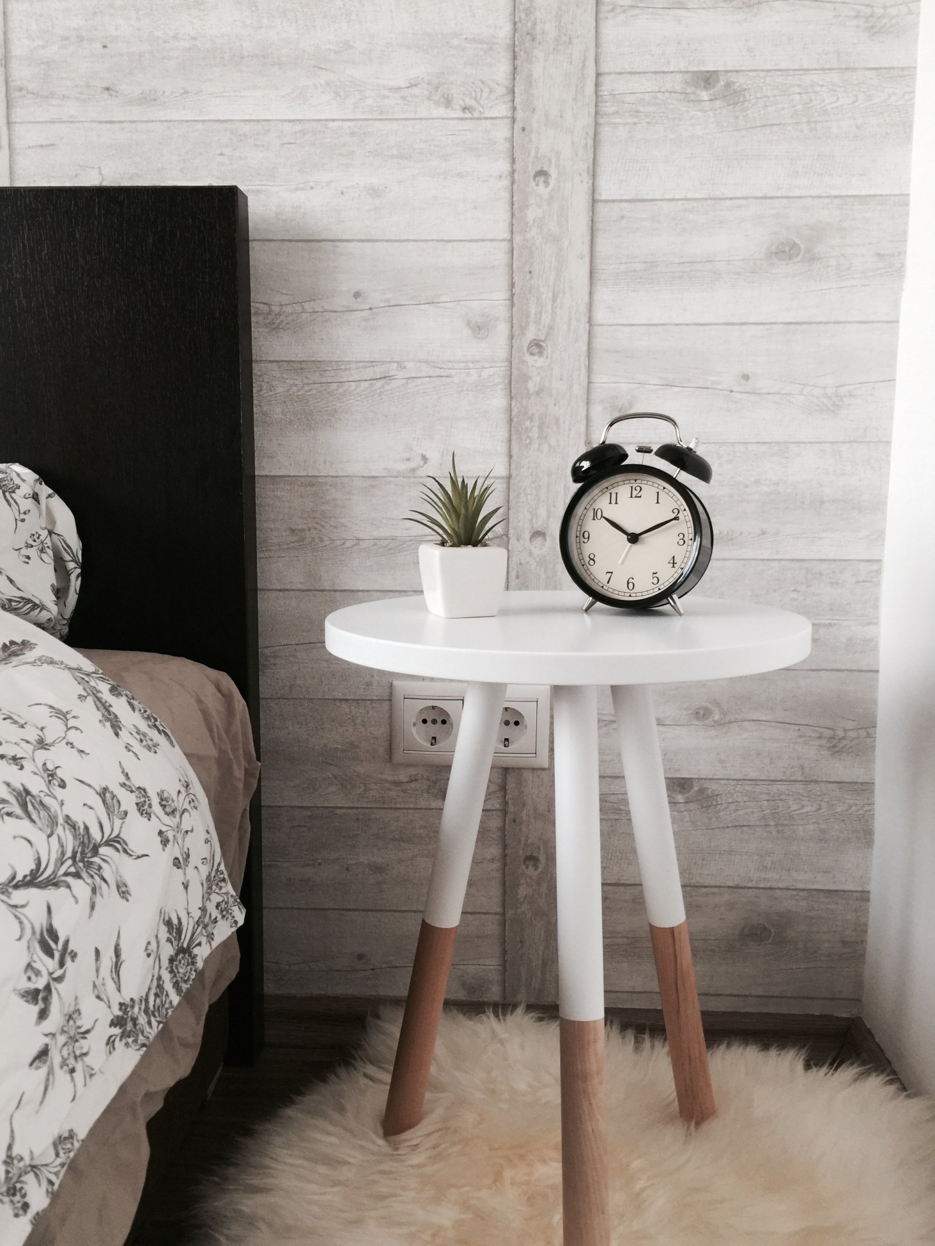 Clock and plant on a white bedside table with three legs