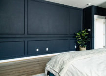 Dark-painted bedroom wall with moldings, green plant, white bed and white doorway