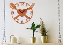 Kitchen wall clock with spoon, fork and heart design hanging on top of a shelf with plants