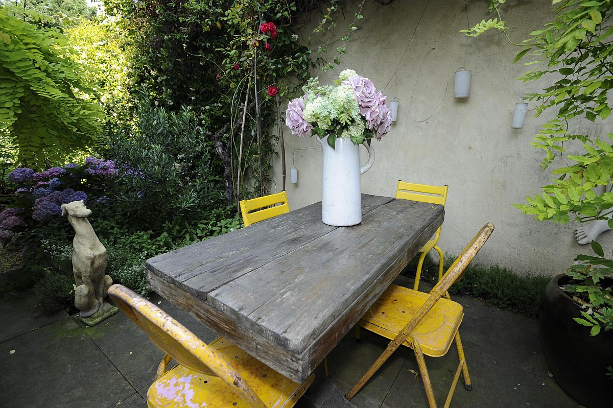 Large rustic wooden table and four colorful chairs in yellow sit at the heart of this shabby-chic patio