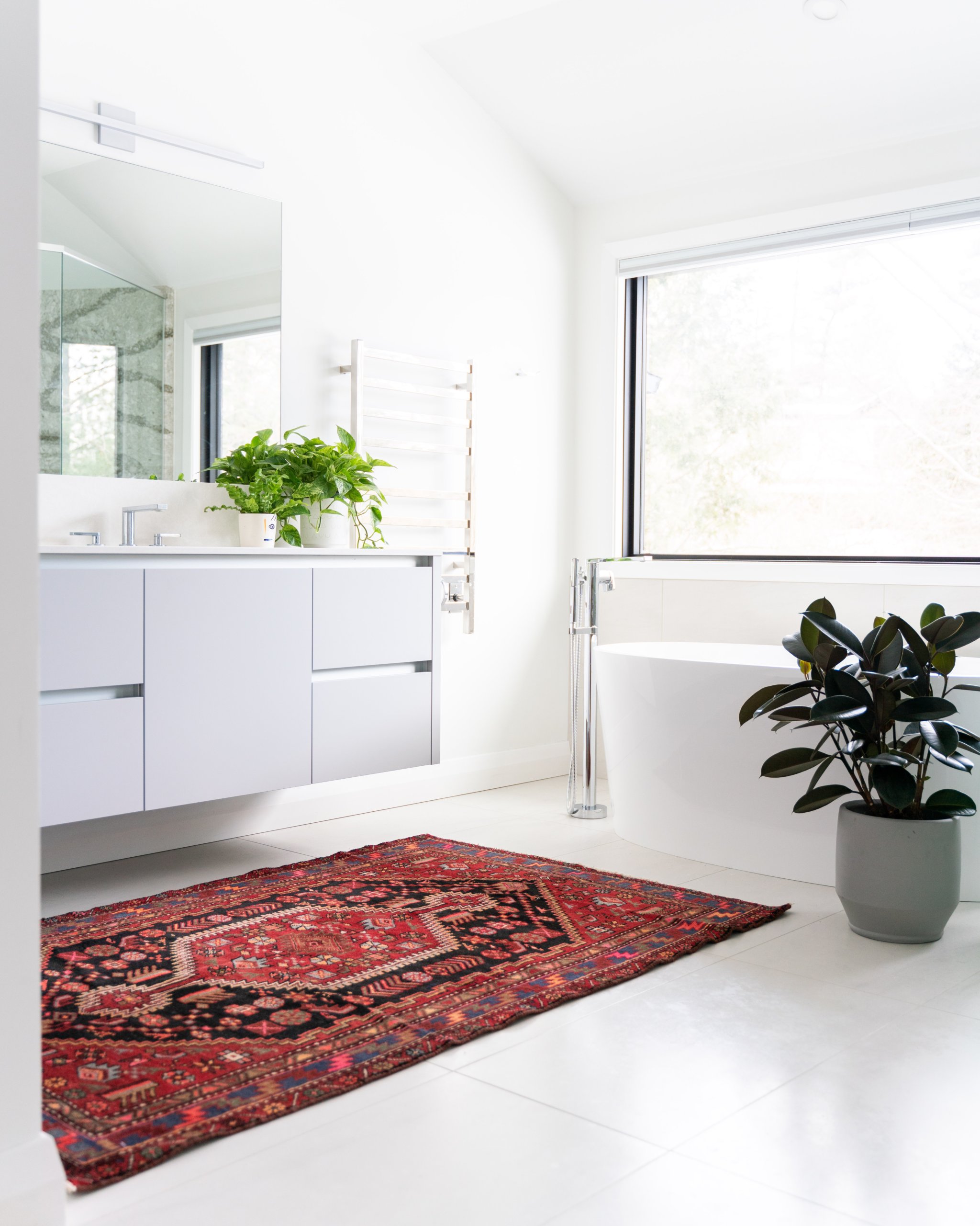 Red patterned rug in an all white bathroom with potted plants