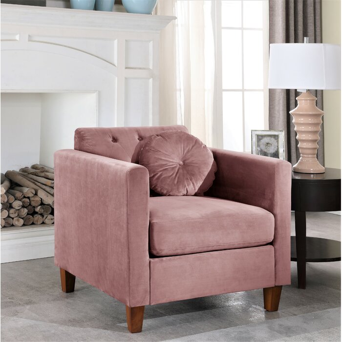 Rose color armchair with round cushion beside a table and a lamp
