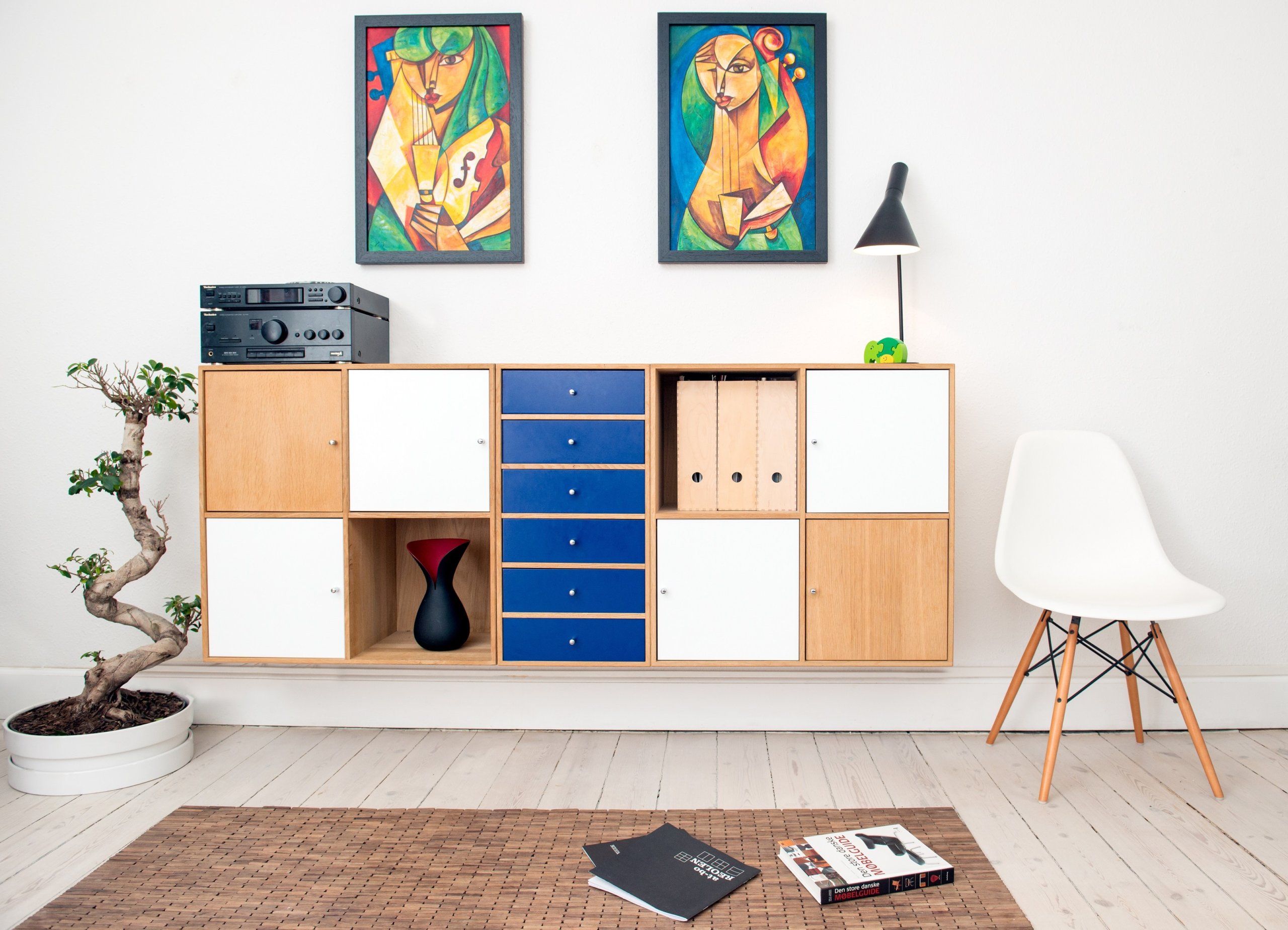 Two paintings above cabinet with blue drawers