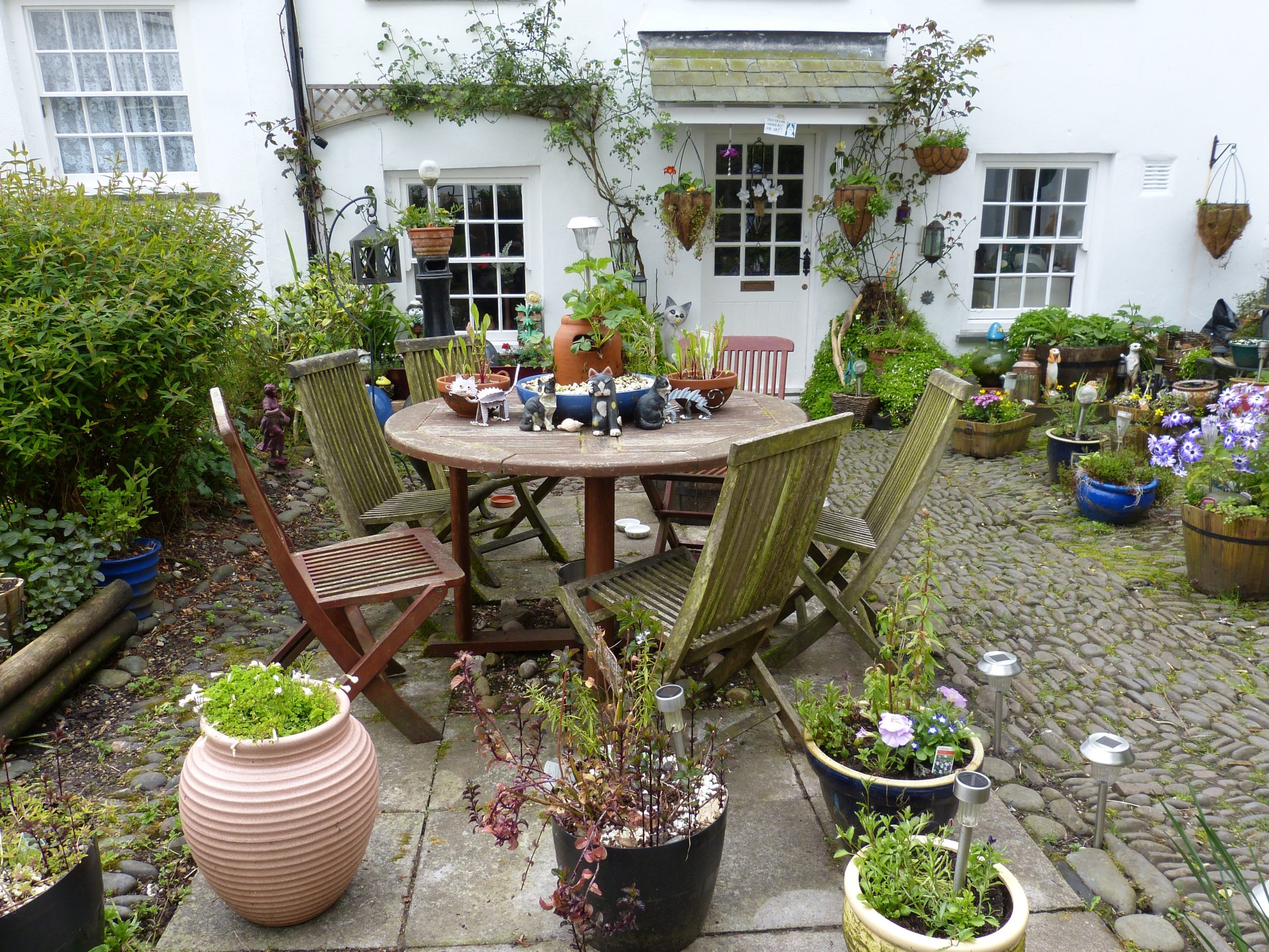 Cottage with table and chairs surrounded by potted plants