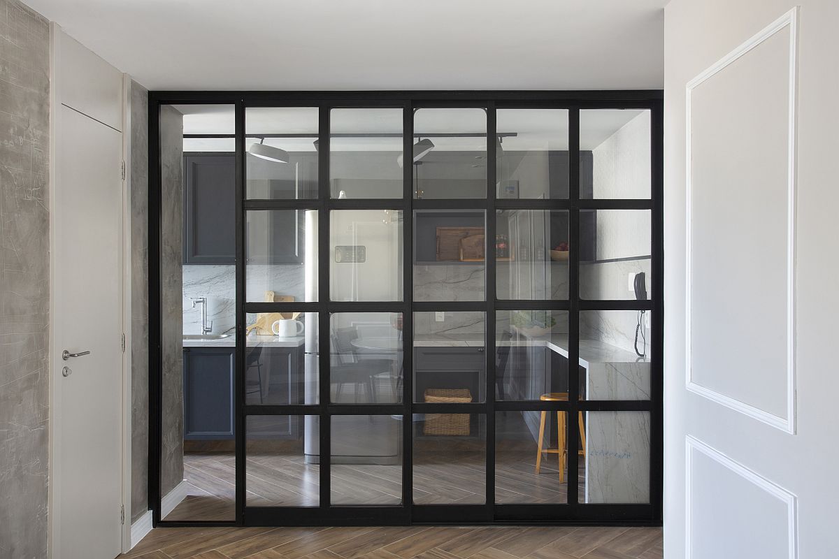 Dark-framed sliding glass doors separate the living area from the kitchen