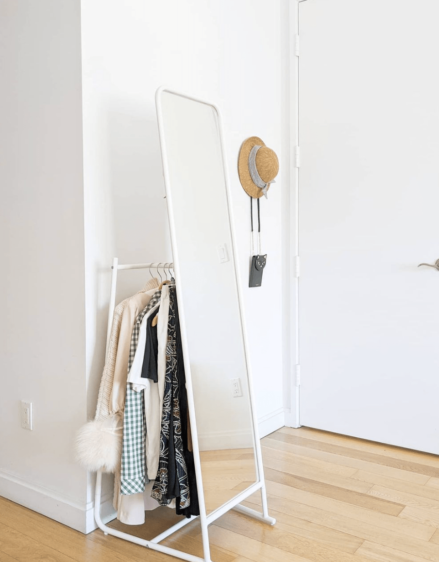 mirror clothing rack white with clothes behind it hat hanging on wall