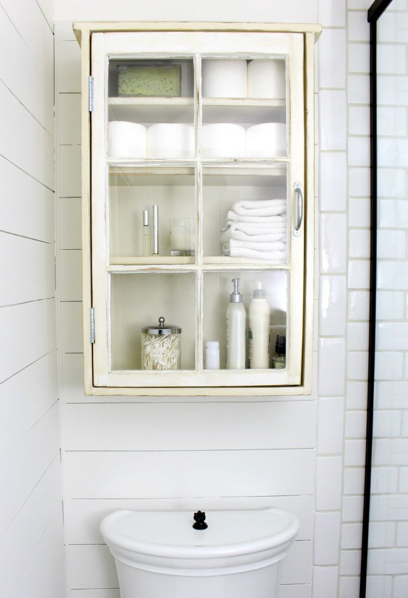 Old white cabinet full of things above toilet