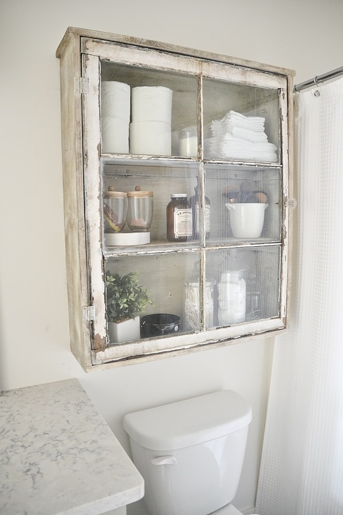 Old white cabinet full of things above toilet