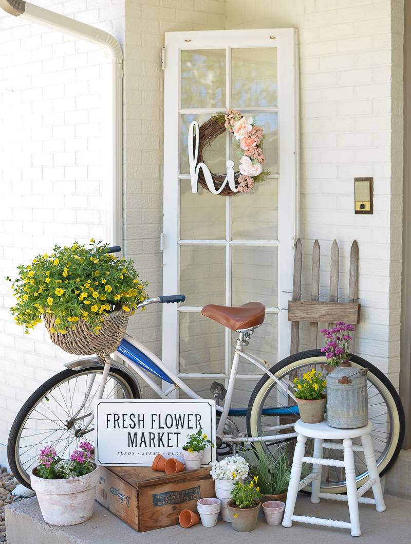 Bike with basket of yellow flowers leaning against white wall