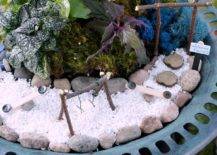 Miniature swing and slides on top of white pebbles surrounded by plants