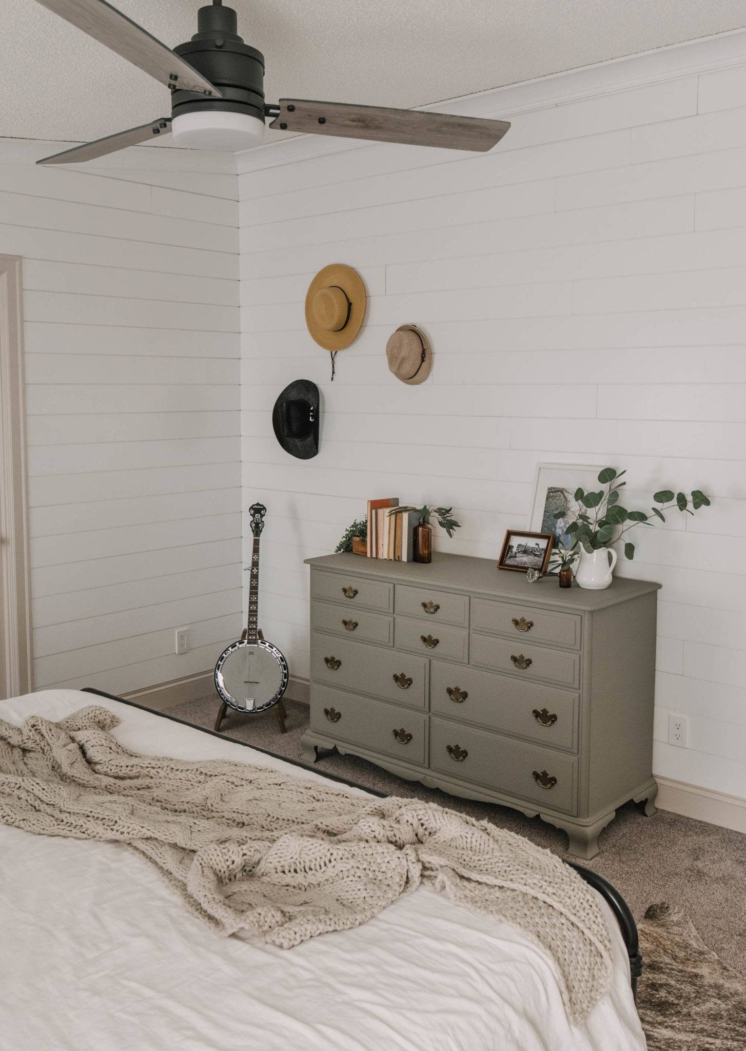 Musical instrument beside a gray drawer cabinet with hats hanging on white wall