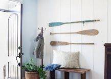 Three paddles on white wall in entryway with bench and cushions