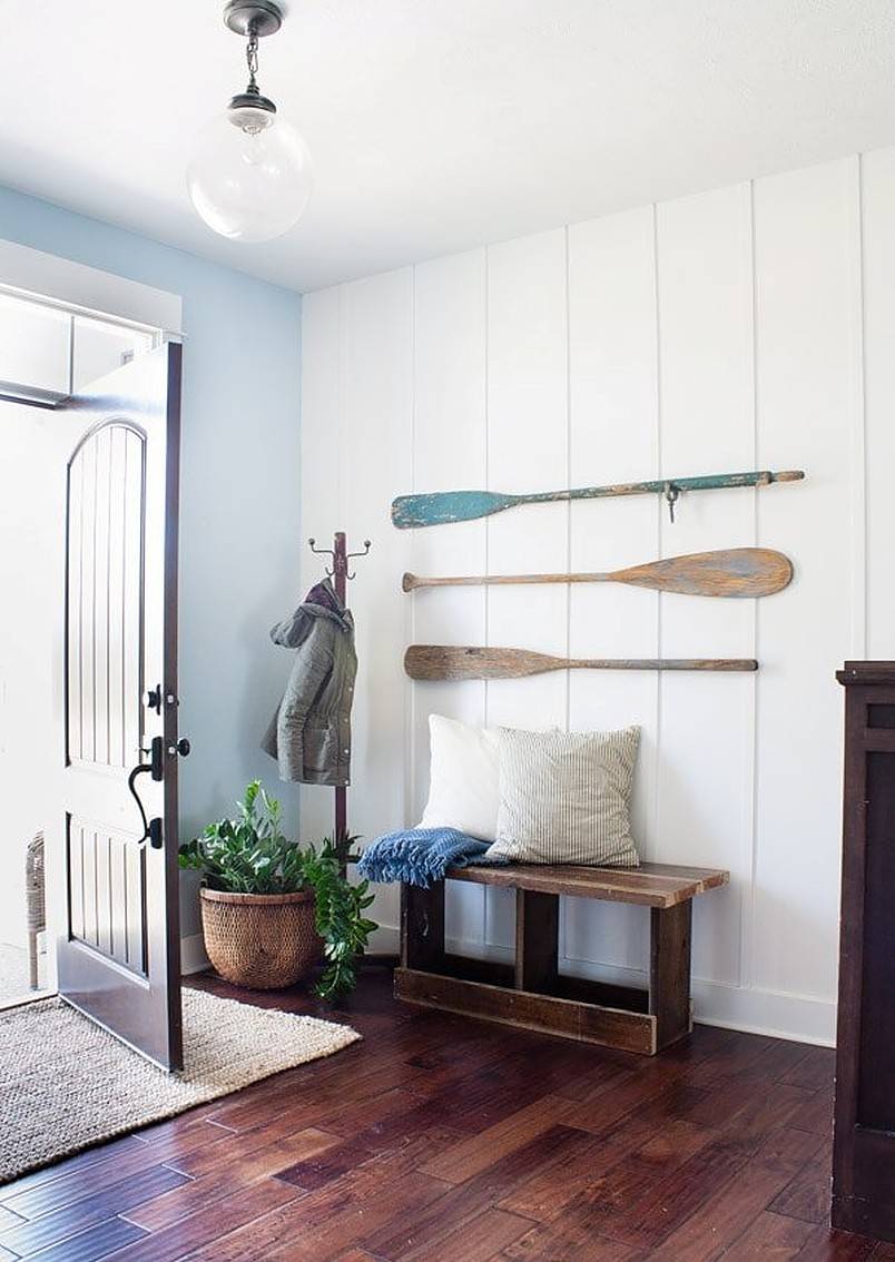 Three paddles on white wall in entryway with bench and cushions