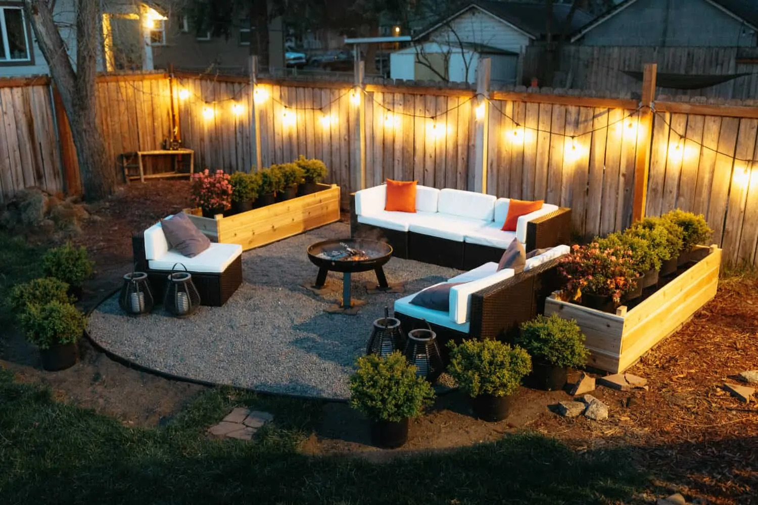 Outdoor firepit surrounded by white sofa with cushions and planters