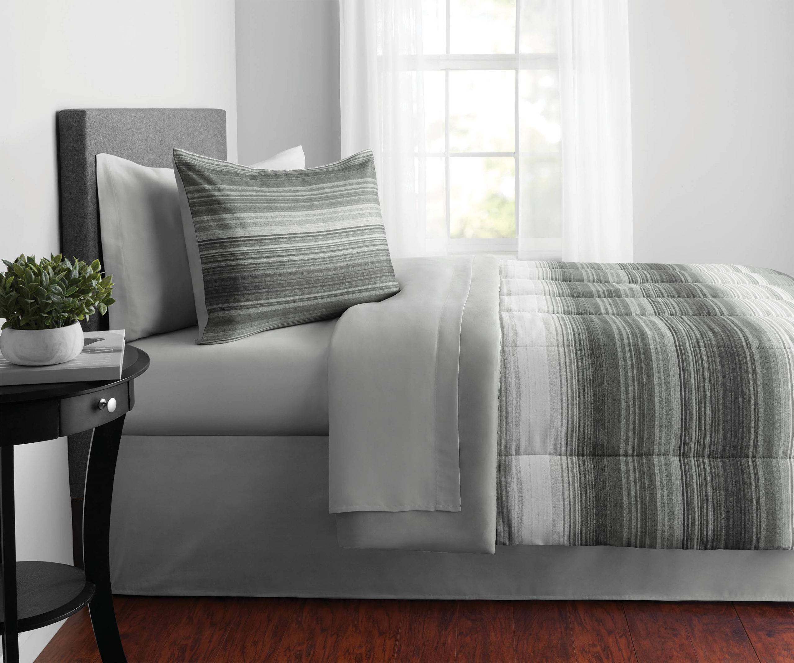 Bed covered in grey sheets with potted plant on the bedside table