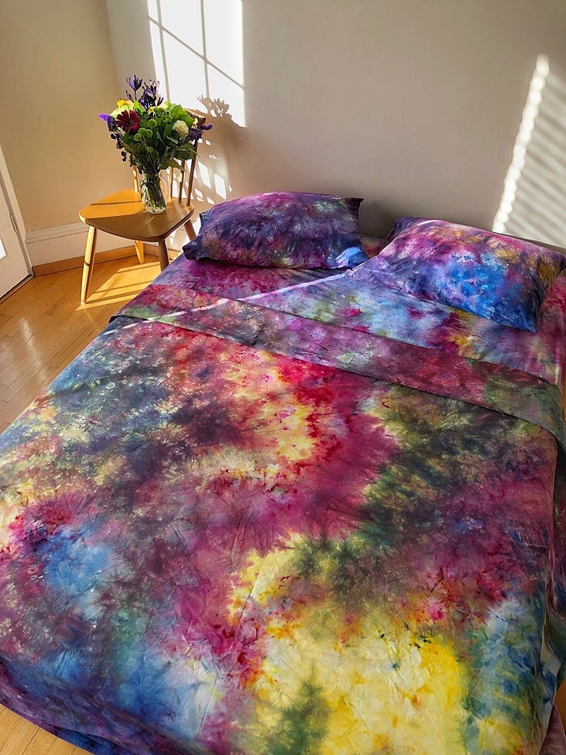 Bed with tie dye sheets and pillows beside a vase full of flowers