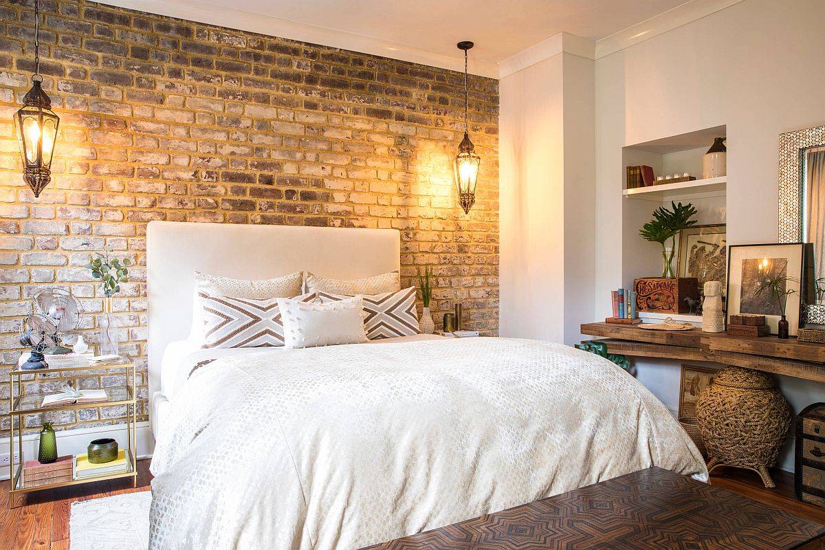 Exposed brick wall in the bedroom is accentuated by the beautiful use of bedside pendants
