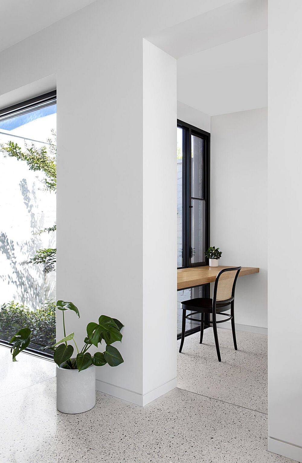 Slim-floating-wooden-desks-at-the-end-of-a-long-open-hallway-with-ample-natural-light-serve-as-workstations-23168