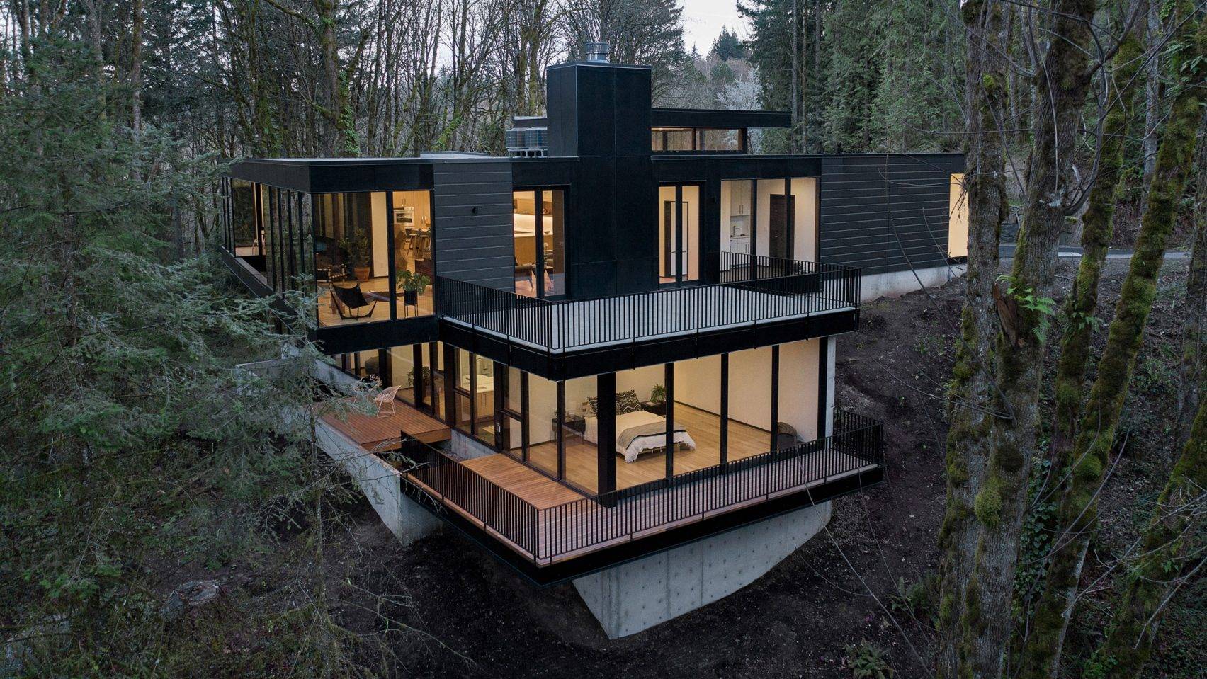 Two-story black house witg glass walls in the middle of the forest