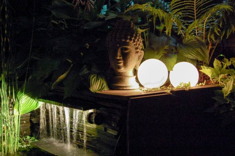 glowing orb lantern next to head sculpture and water feature