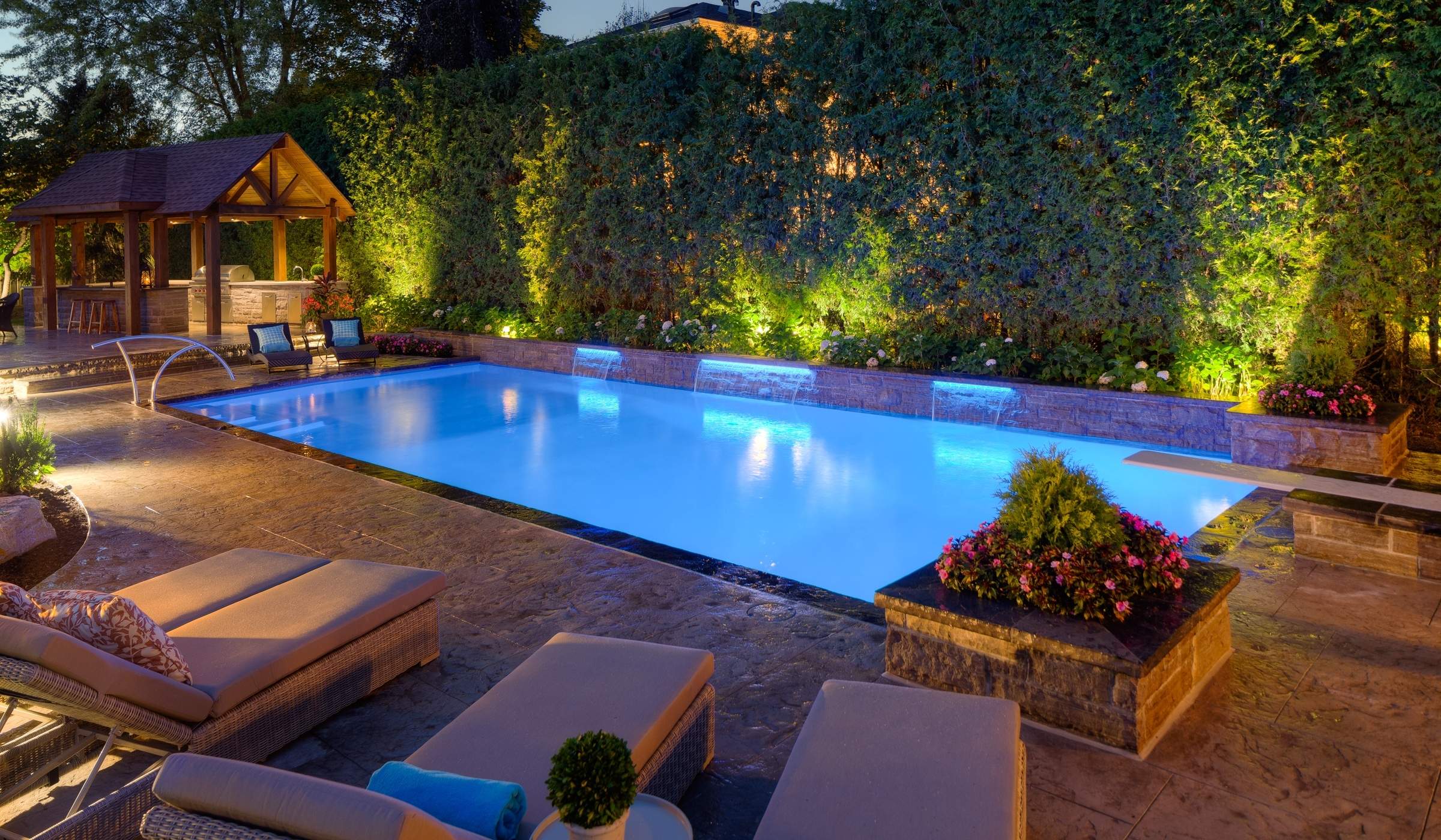 in ground pool at night lit up with stone patio and water feature