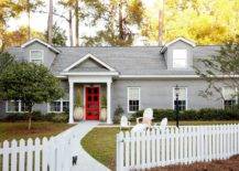 white picket fence in front of grey home with red door
