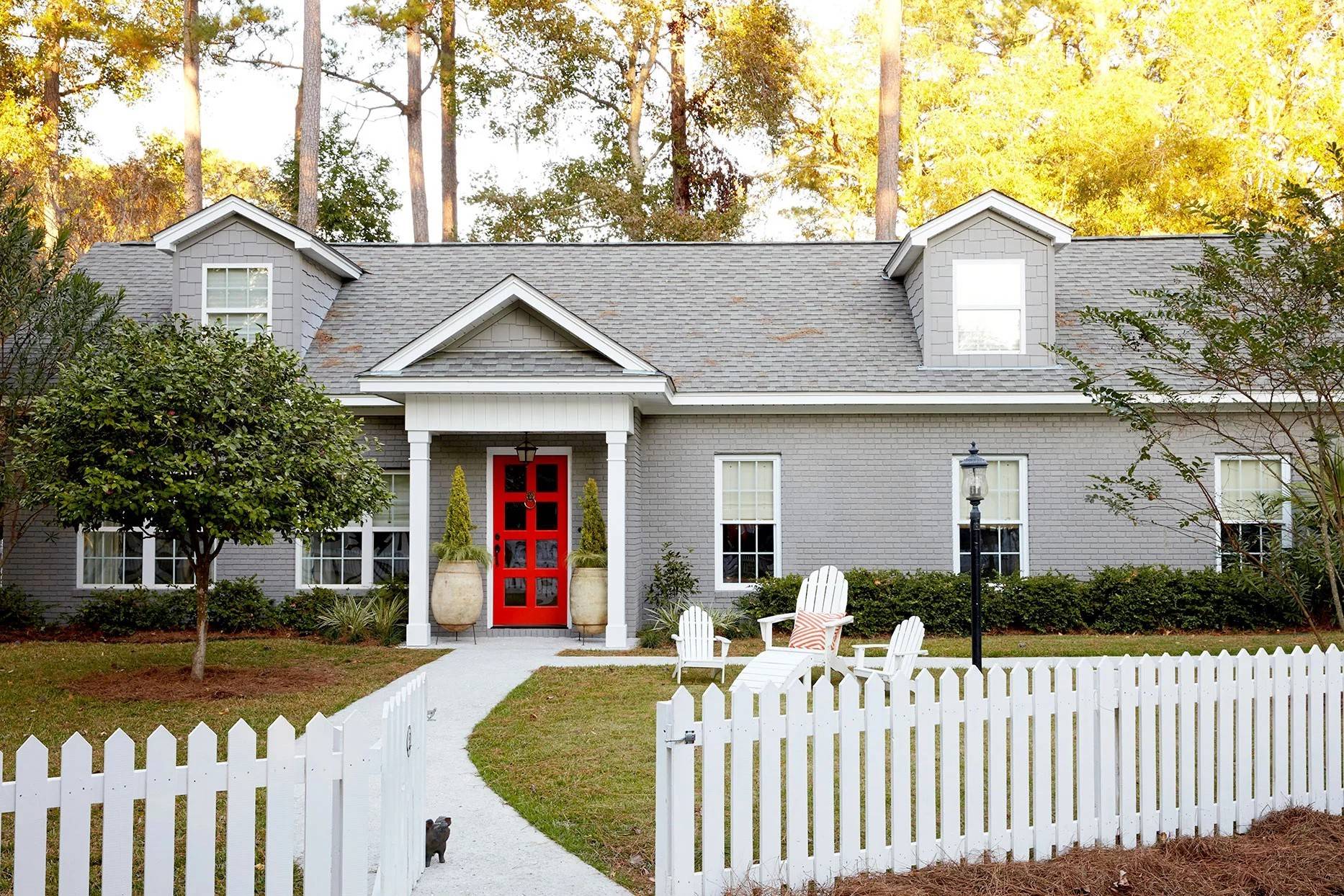 white picket fence in front of grey home with red door