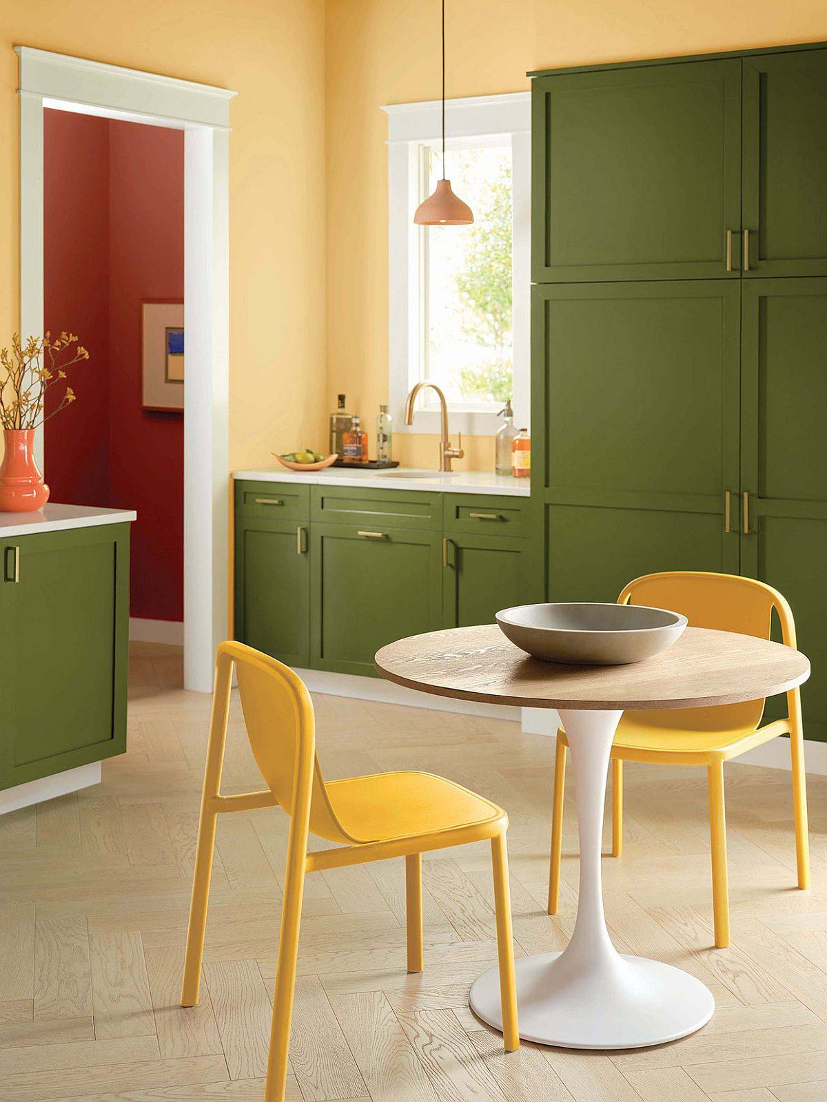 Gorgeous green cabinets coupled with yellow in the midcentury modern kitchen with a pedastal dining table