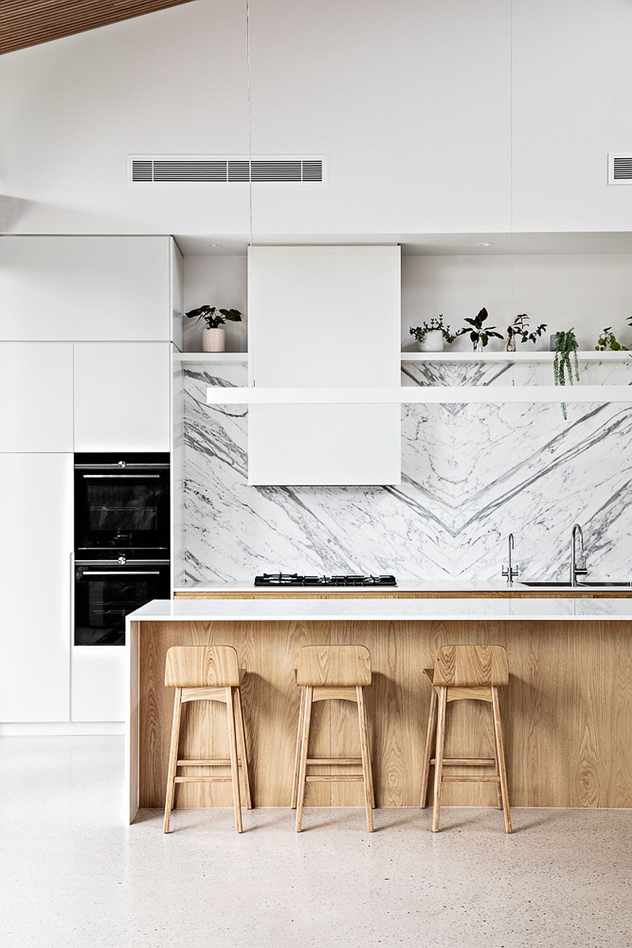 Lovely white marble backsplash steals the show in this kitchen with wooden cabinets and island