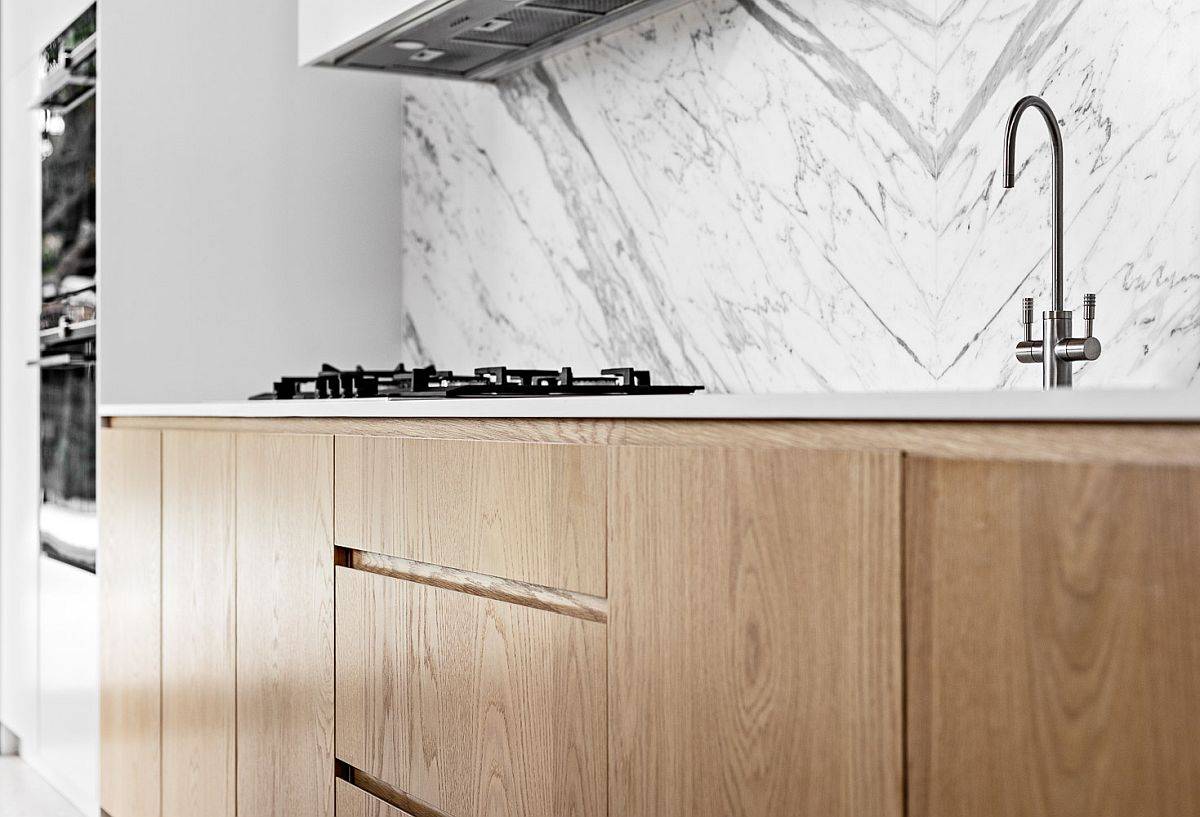 Minimal wooden cabinets of the kitchen complement the marble backsplash beautifully in here