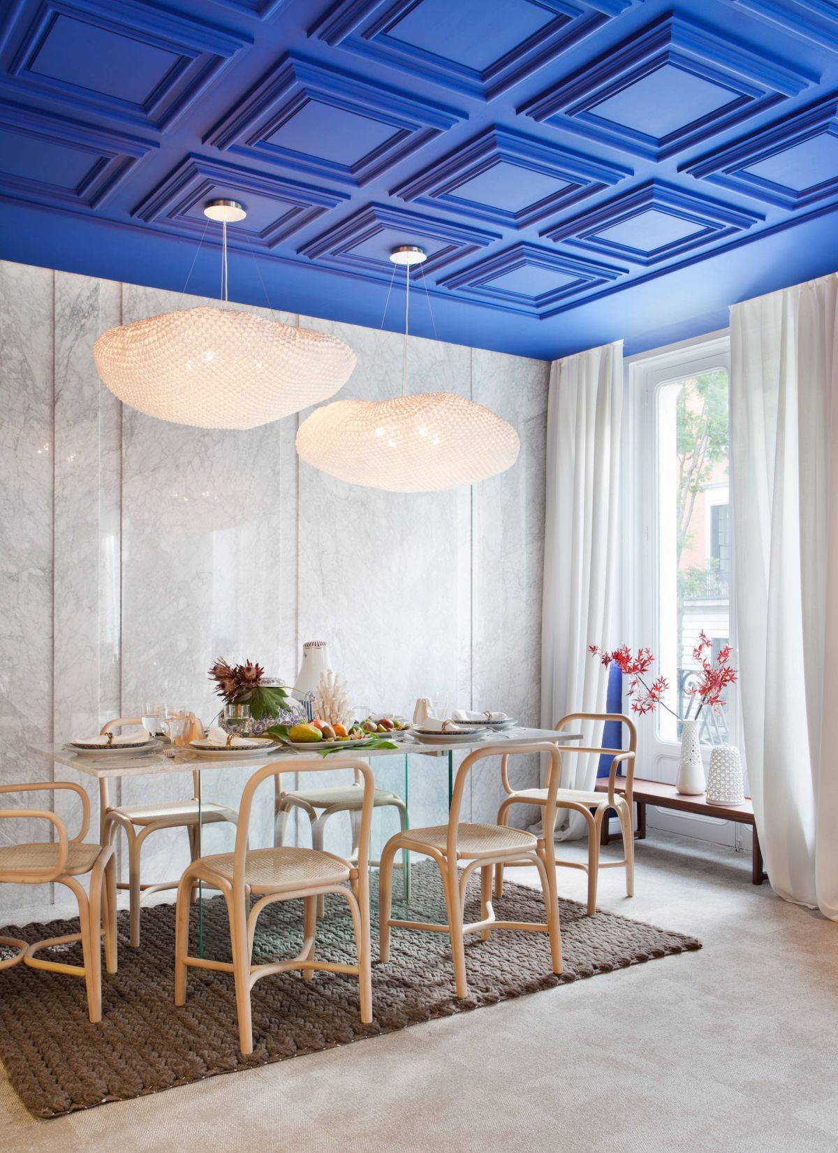 Coffered ceiling in deep blue adds color to this double-height dining room in white