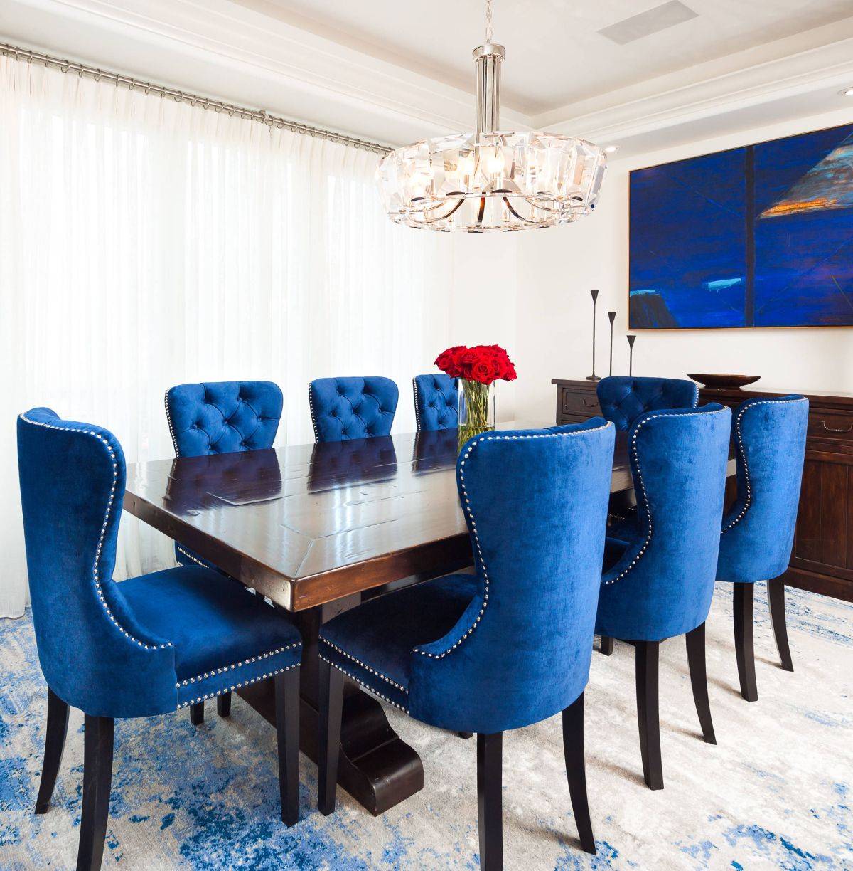 Wall art in deep blue perfectly complements the colorful chairs in this white dining room