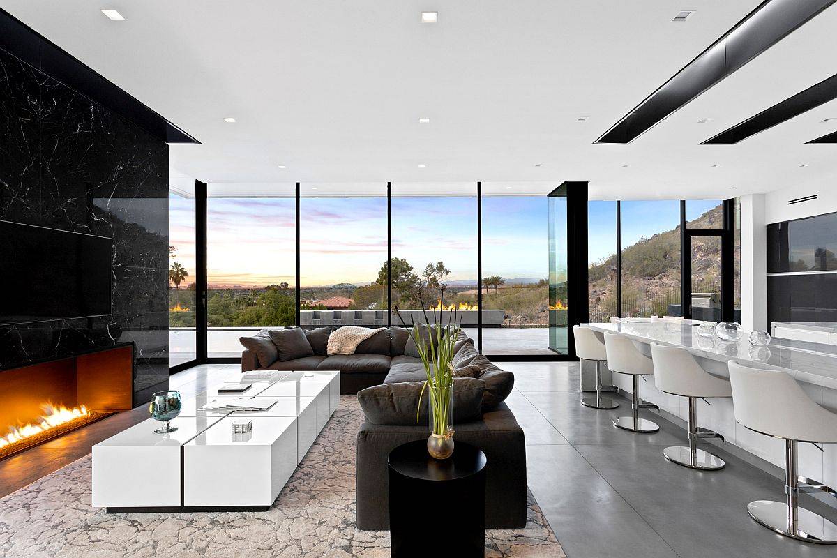 Stunningly beautiful living room of the home with floor-to-ceiling glass walls and a polished, dark stone fireplace