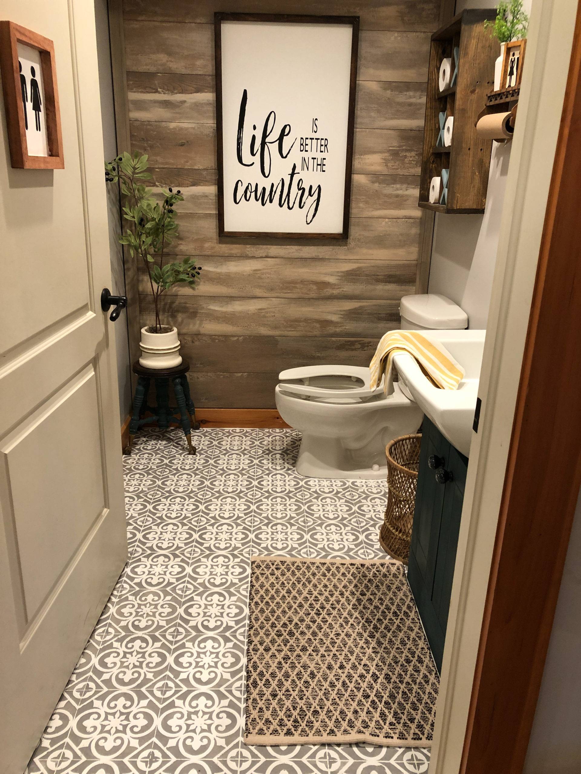 country bathroom farmhouse wood accent wall stenciled tile floor toilet greenery sign