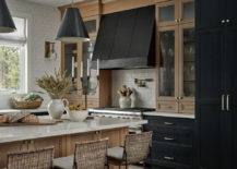 dark kitchen light wood cabinetry pendants oven range hood island stools
