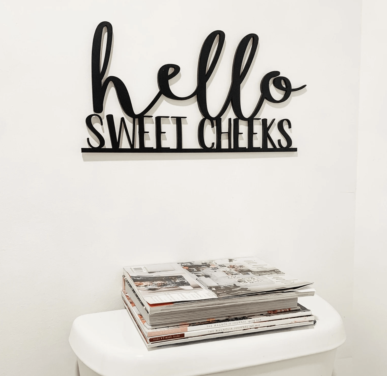 hello sweet cheeks black iron cut out bathroom sign hanging over toilet stack of magazines