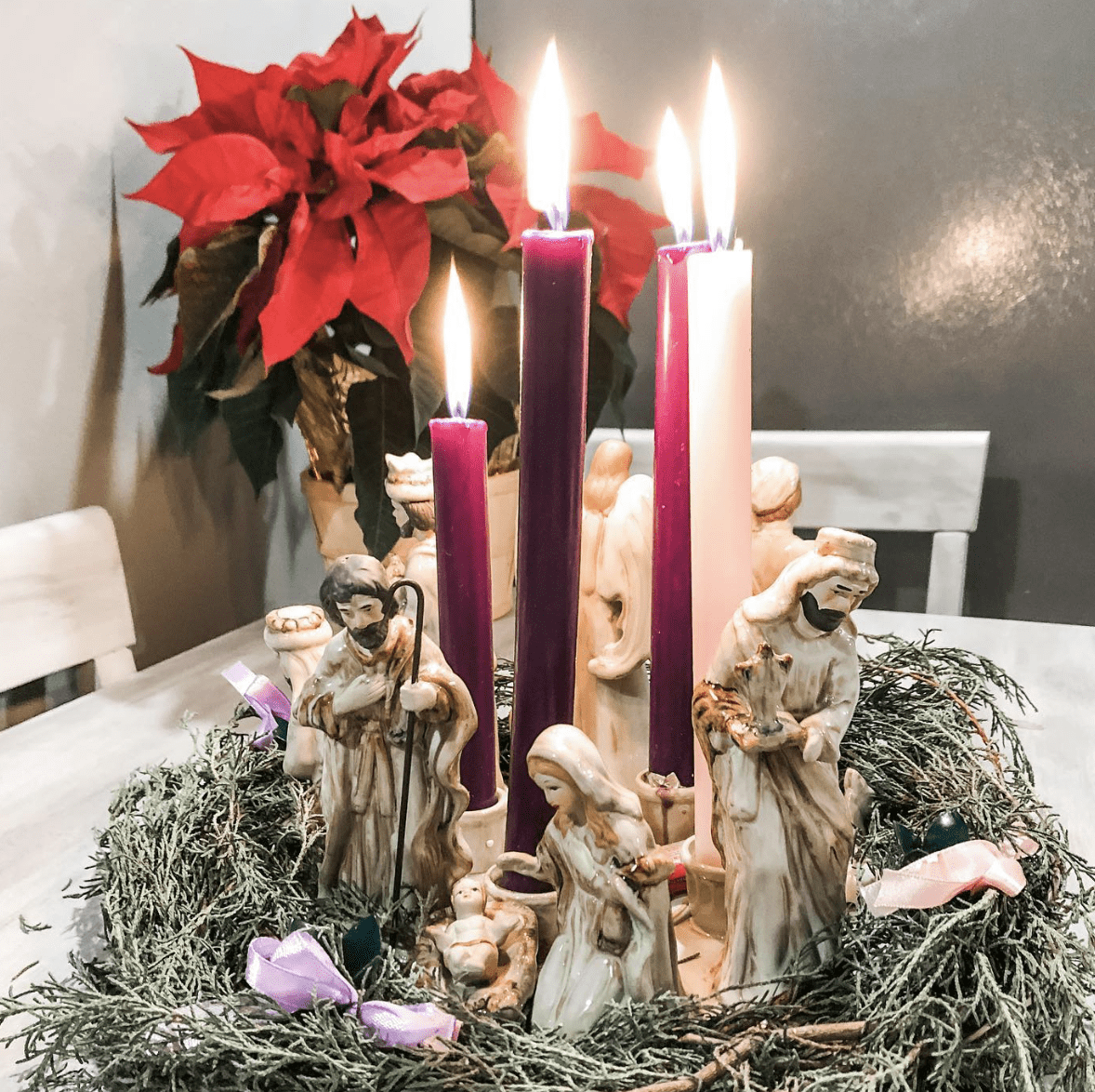 advent wreath purple and pink candles with nativity figurines poinsettia in background