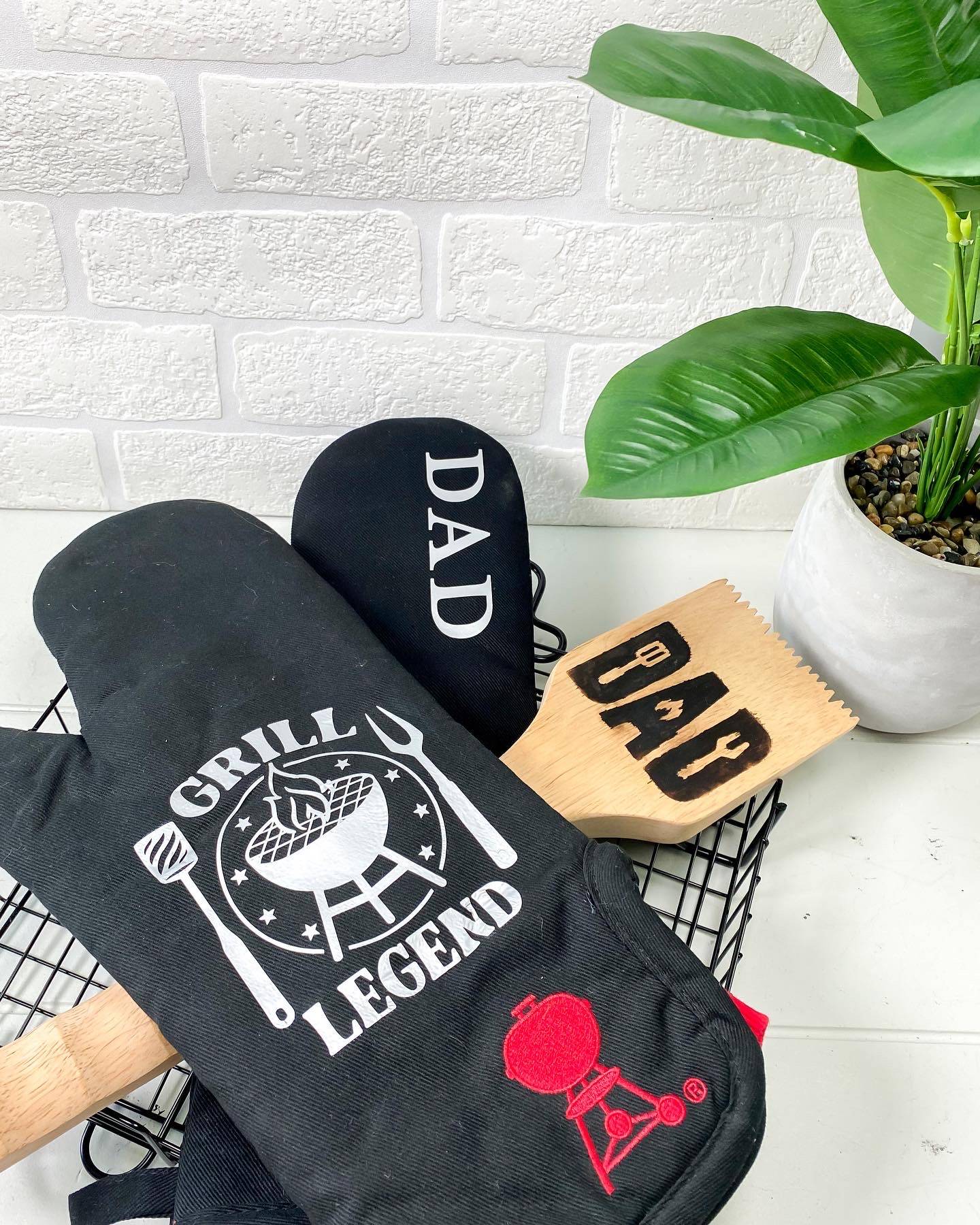 black oven mitts dad father's day gift idea wood bbq scraper white brick background plant wire basket