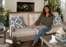 cindy crawford sitting on a outdoor couch with pillows in front of fireplace