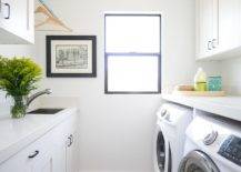 white laundry room side by side washer dryer golden rod jar sink black frame window clothes drying rod white shaker cabinets